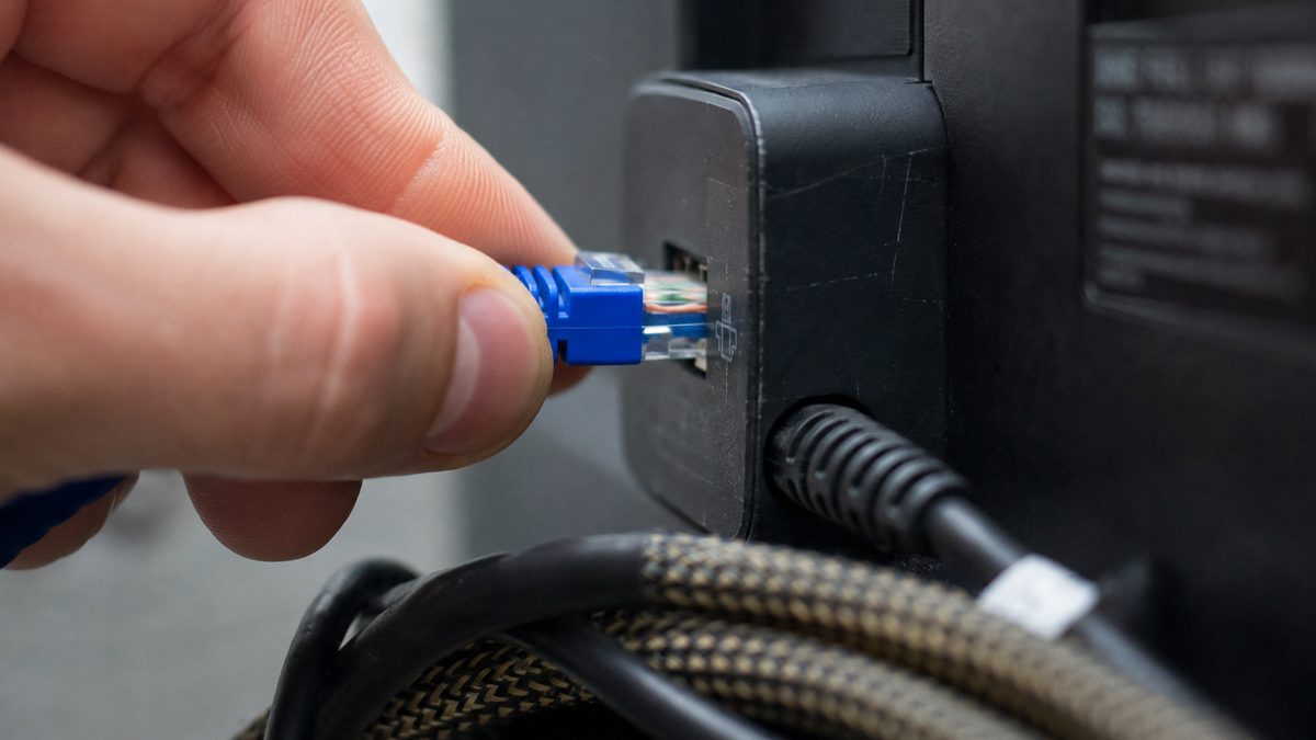 Ethernet cable being plugged into a small streaming device behind a television