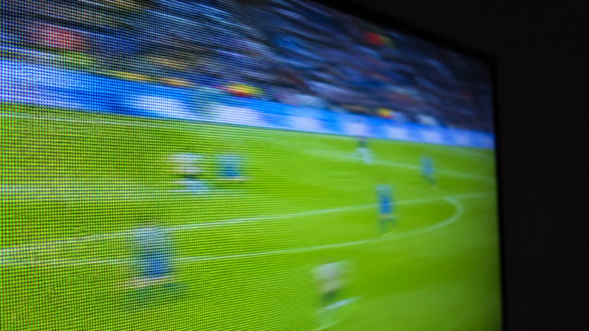 Close-up of a television screen showing a live football match with a scoreboard overlay
