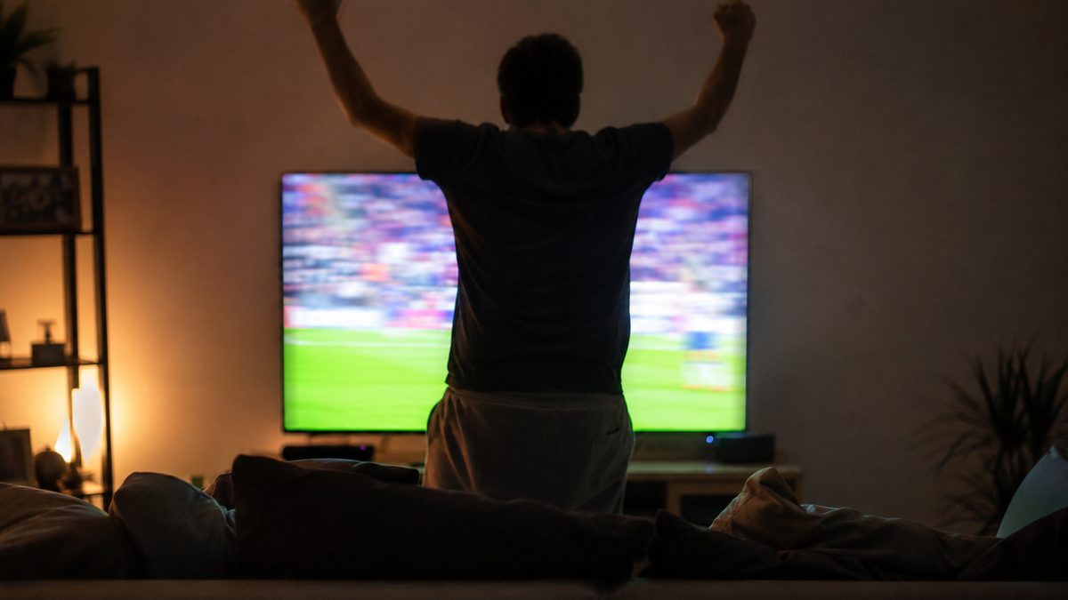 Person celebrating a goal in front of a television in a dark living room